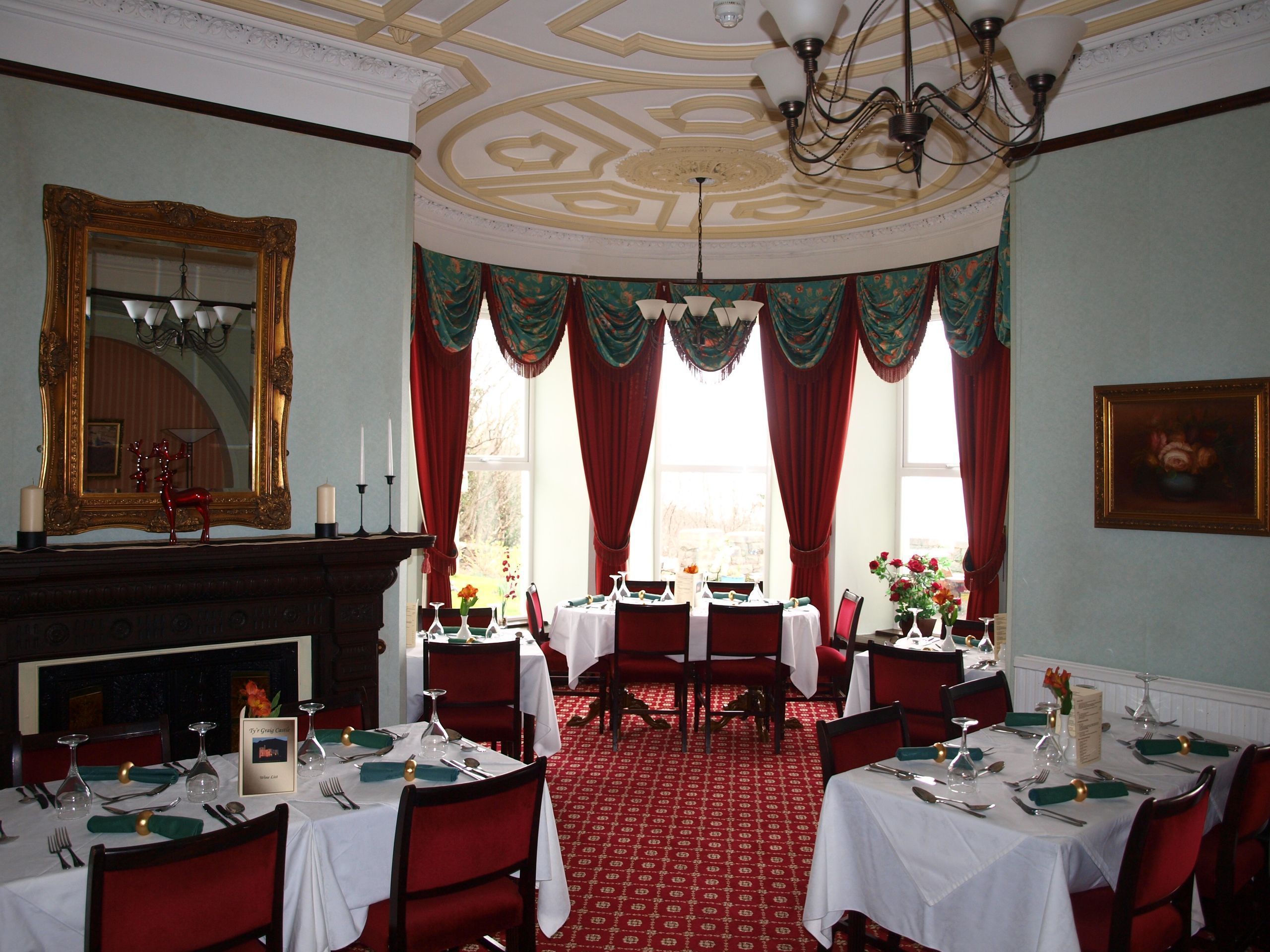 Een eetkamer met gedekte tafels, een open haard en een grote spiegel aan de muur.