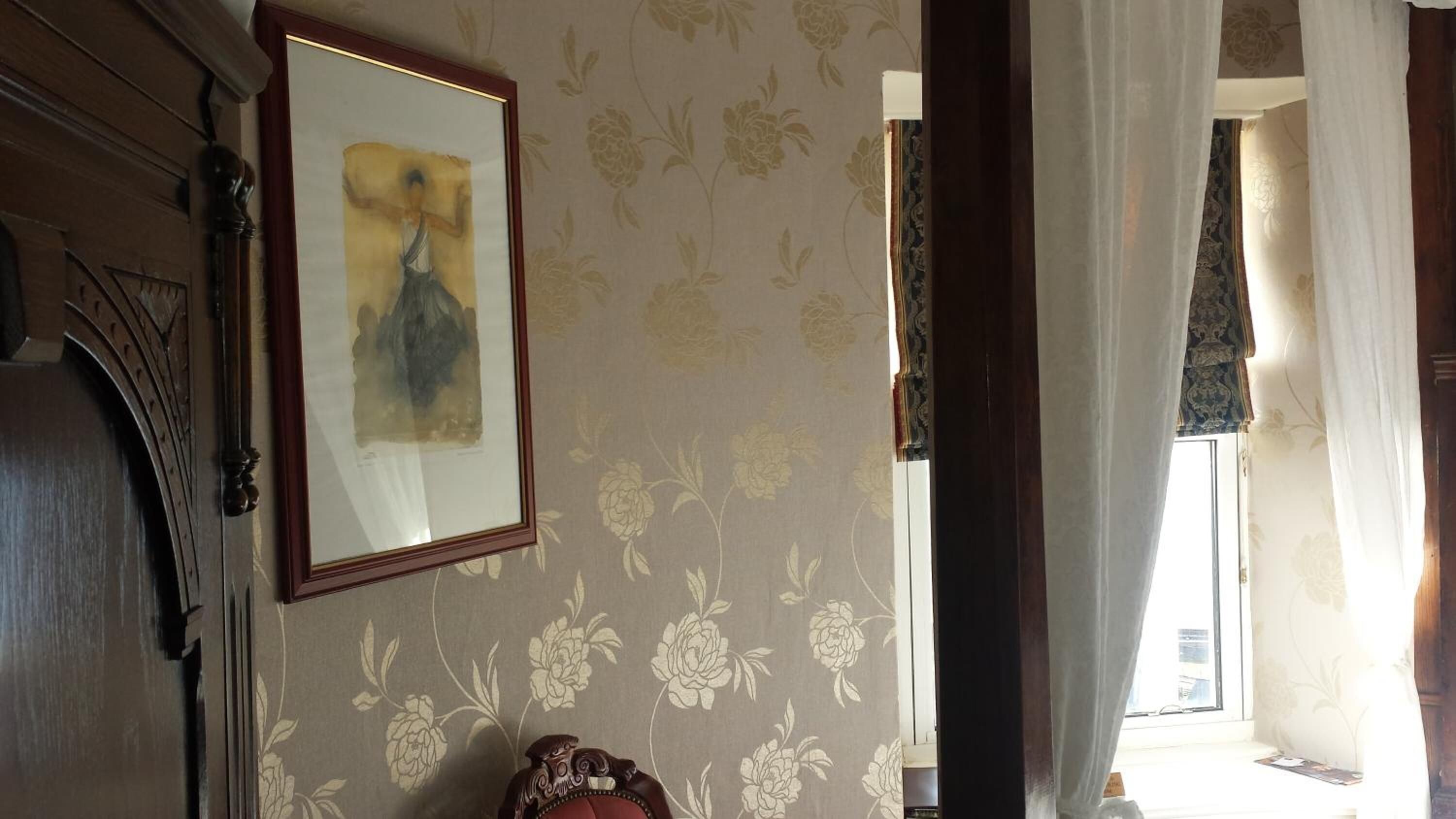 Una habitación con papel tapiz floral, una obra de arte enmarcada en la pared y una puerta con picaporte decorativo.
