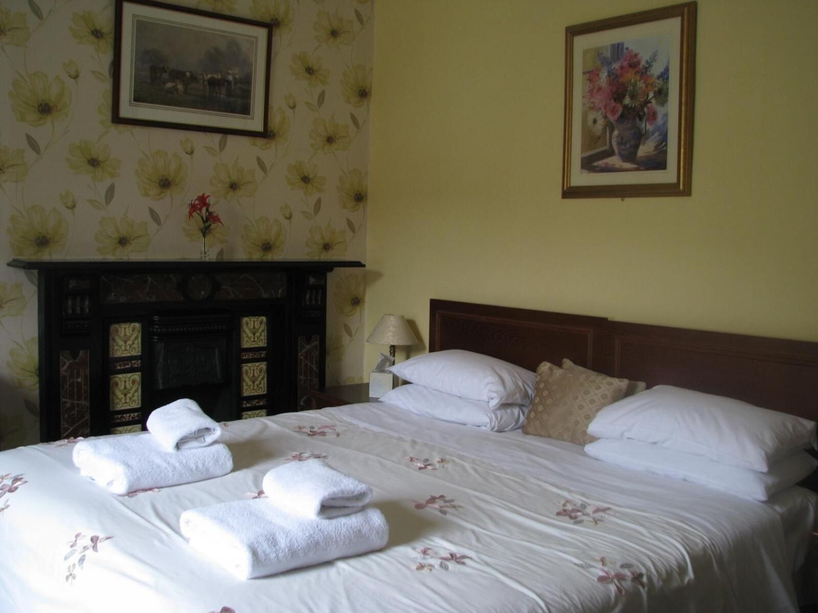 Habitación de hotel con cama, papel tapiz floral, chimenea y dos cuadros en la pared.