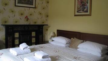 Ein Hotelzimmer mit Bett, Blumen-Tapete, Kamin und zwei gerahmten Bildern an der Wand.