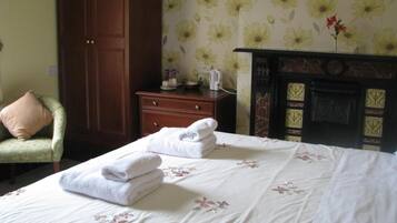 A hotel room with a bed, a wooden dresser, a green armchair, and a fireplace.