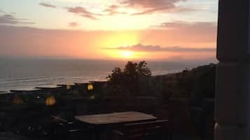 A sunset view from a terrace with a table and chairs, overlooking the sea.
