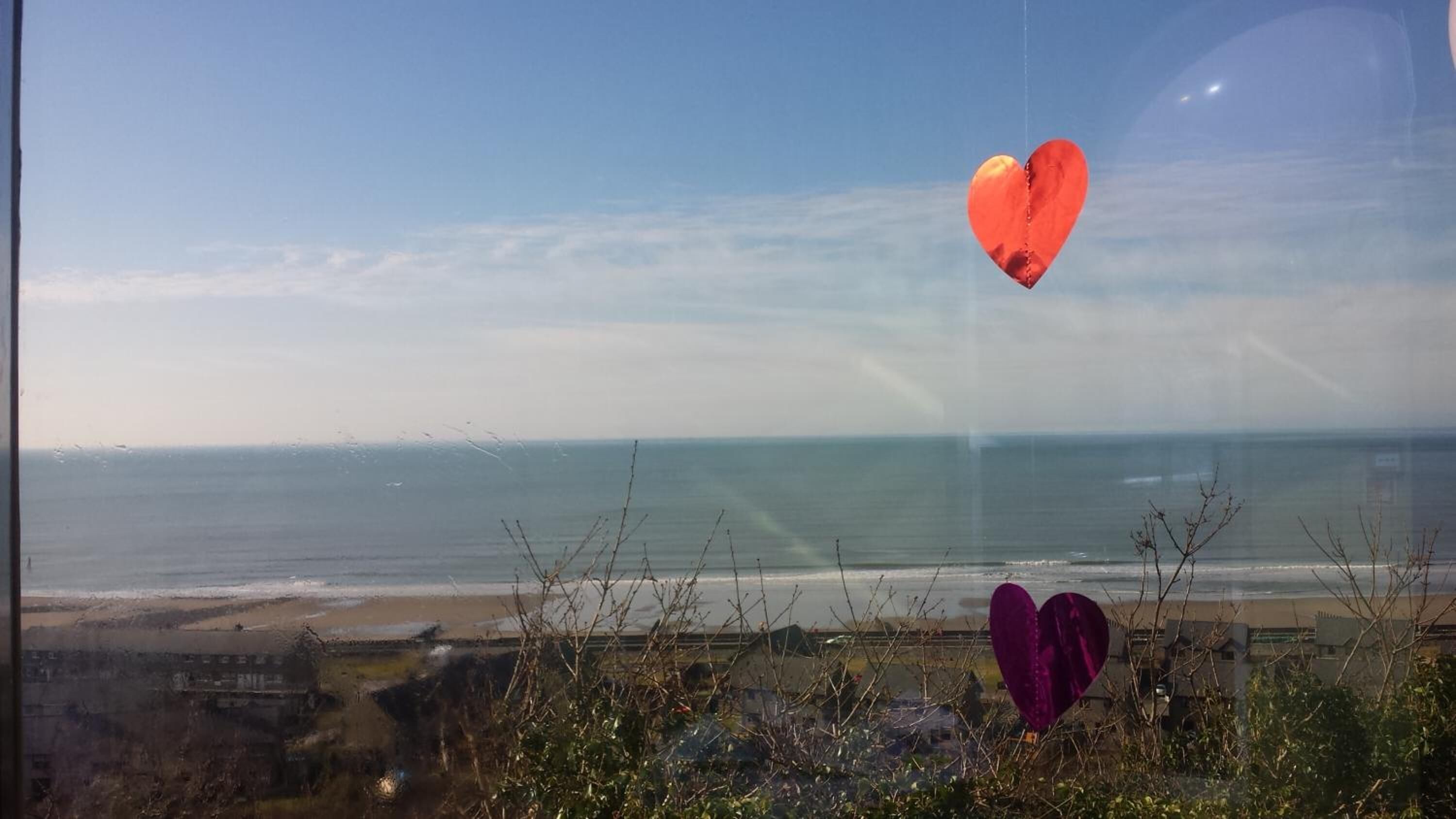 A view of the ocean from a window with two heart-shaped decorations.