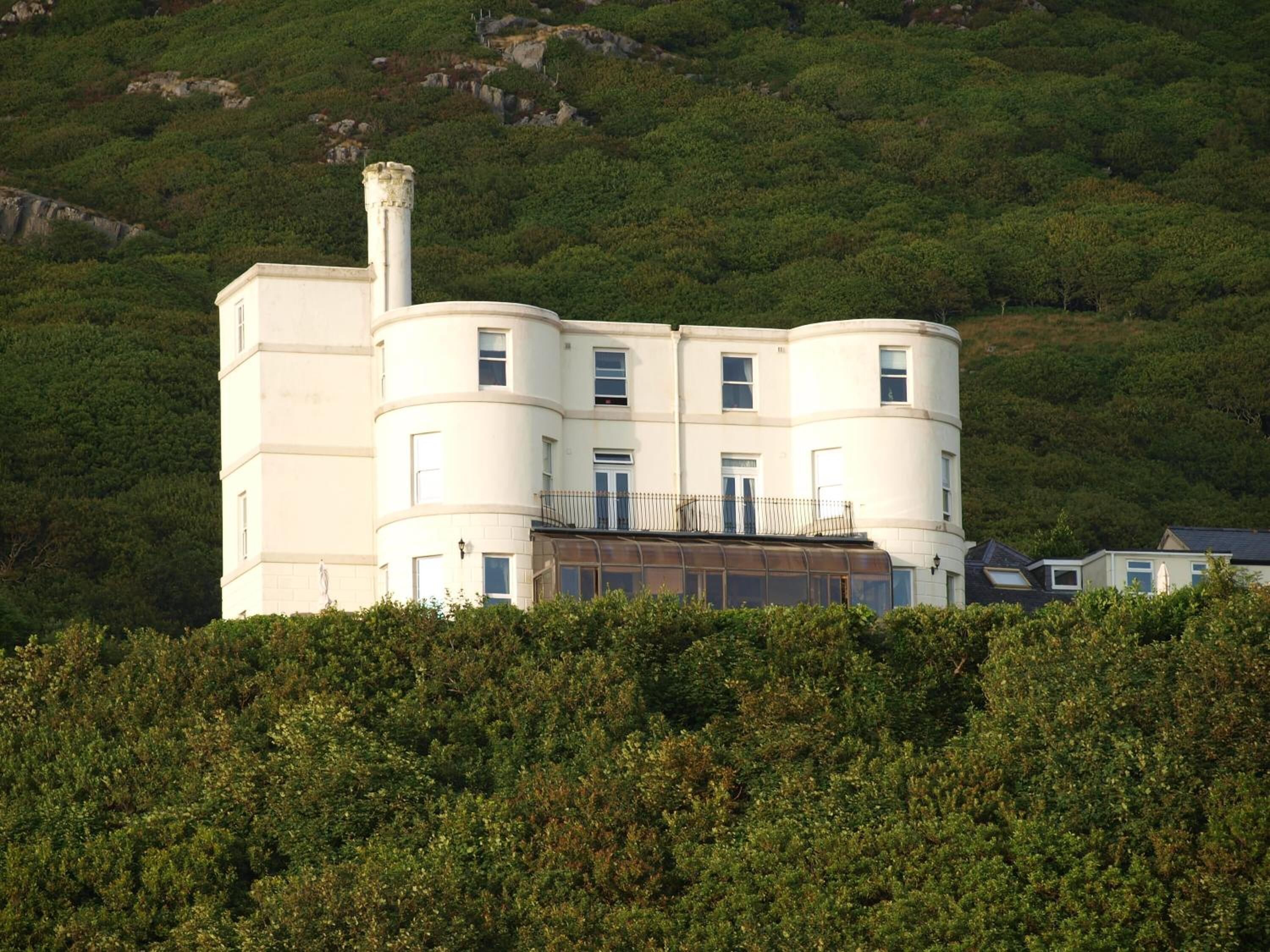 A multi-story building with a cylindrical section and a chimney, surrounded by dense greenery.