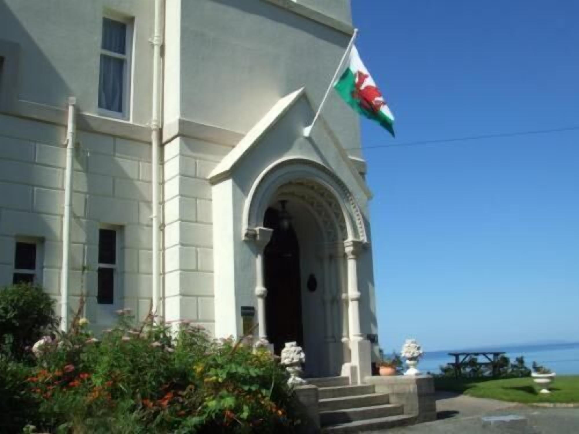 Un edificio con una amplia entrada arqueada, una bandera y vistas al mar.