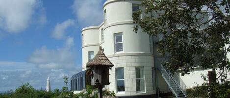 A large, white, multi-story building with a turret and a staircase on the right side.