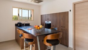 Una cucina moderna con un'isola centrale, sedie in legno, una ciotola di frutta e una vista dalla finestra.