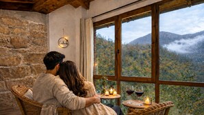 A couple sitting by a window overlooking a mountainous landscape, with a stone wall and a small table with candles and glasses. - Romantic place with Jacuzzi, fantastics mountain Views And Fireplace (Asturias)