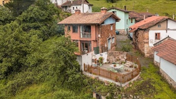 Un pueblo en una ladera con casas tradicionales, un patio central con una mesa y sillas, y un muro de piedra.