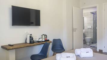 Une chambre d’hôtel équipée d’un téléviseur à écran plat, d’un bureau en bois avec une machine à café, de deux chaises et d’un lit avec des serviettes soigneusement pliées.