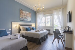 A hotel room with two beds, a desk, and a chair. There is a painting on the wall, a chandelier, and a window with curtains. - Trastevere Gallery Suites (Rome)
