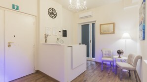 A reception area with a white reception desk, two chairs, a chandelier, a clock, and a framed mirror.
