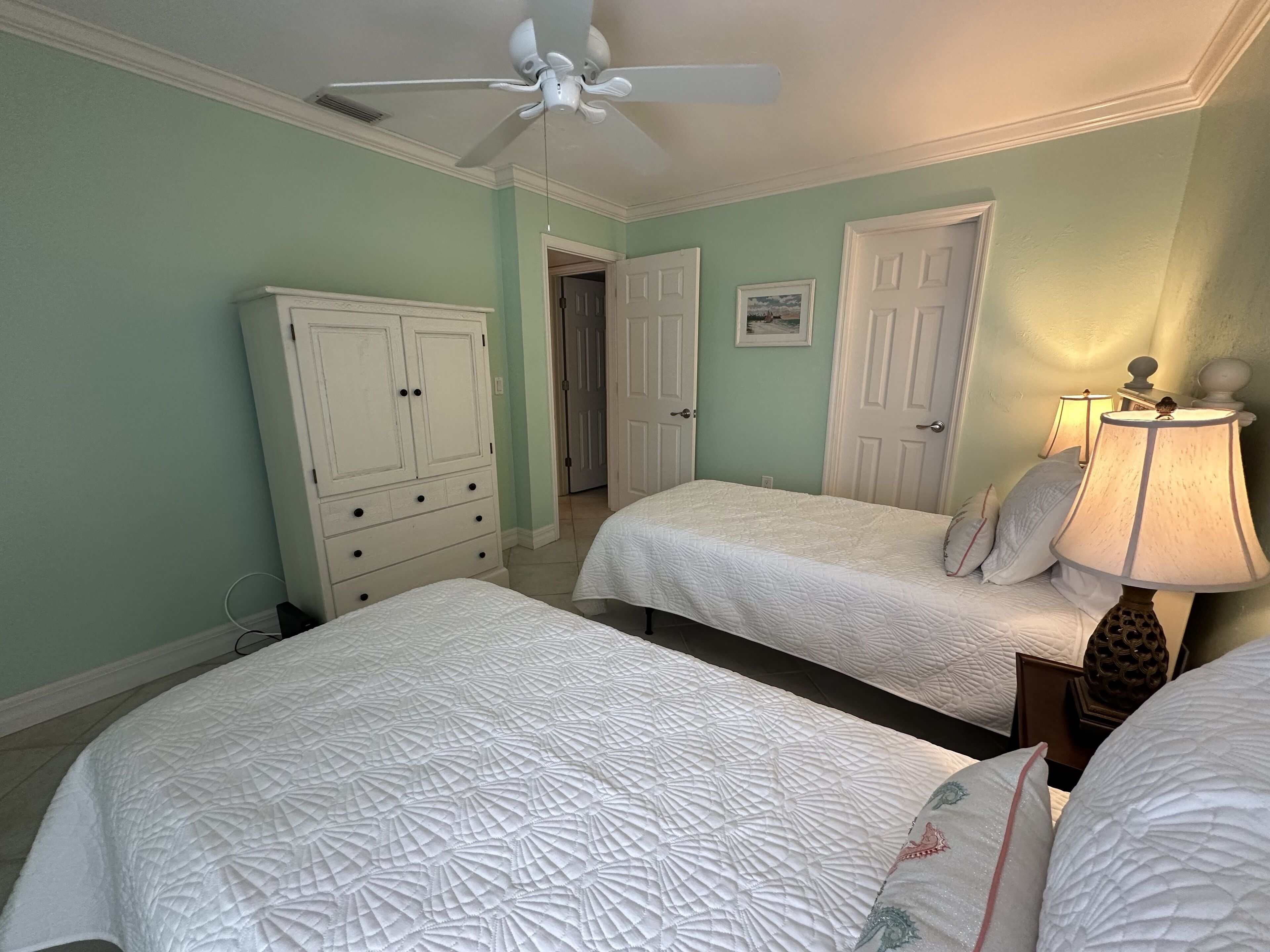 A bedroom with two beds, a ceiling fan, and a dresser.