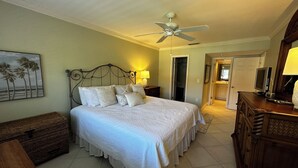 A bedroom with a bed, a ceiling fan, a nightstand, a dresser, a lamp, and a painting on the wall. - Enjoy the tranquility of this spacious two bedroom unit. Siesta Dunes 6-203 (Siesta Key)