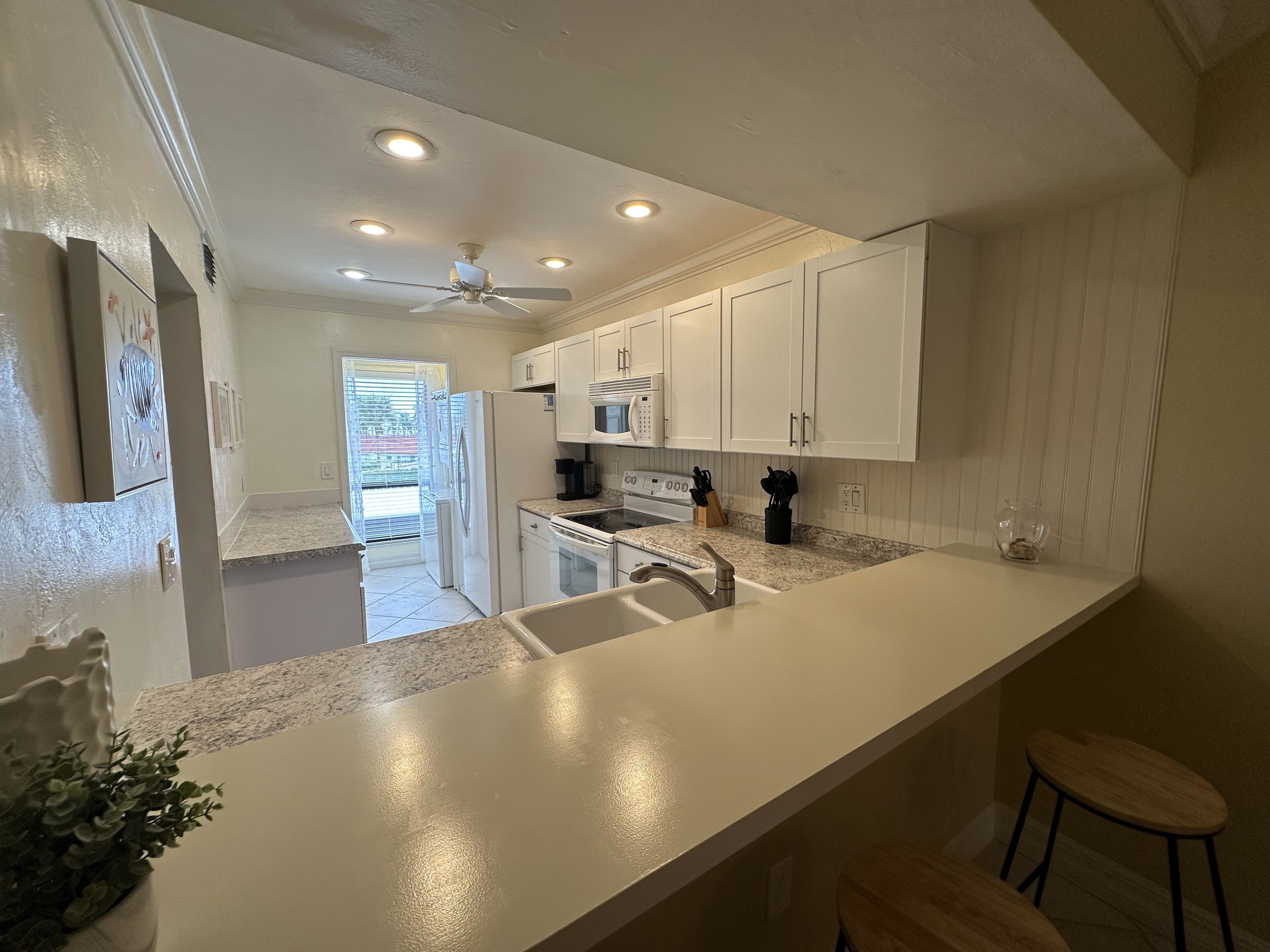 A kitchen with white cabinets, a granite countertop, a built-in oven, and a ceiling fan.