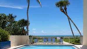 Piscina com espreguiçadeiras e palmeiras, com vista para um corpo de água.