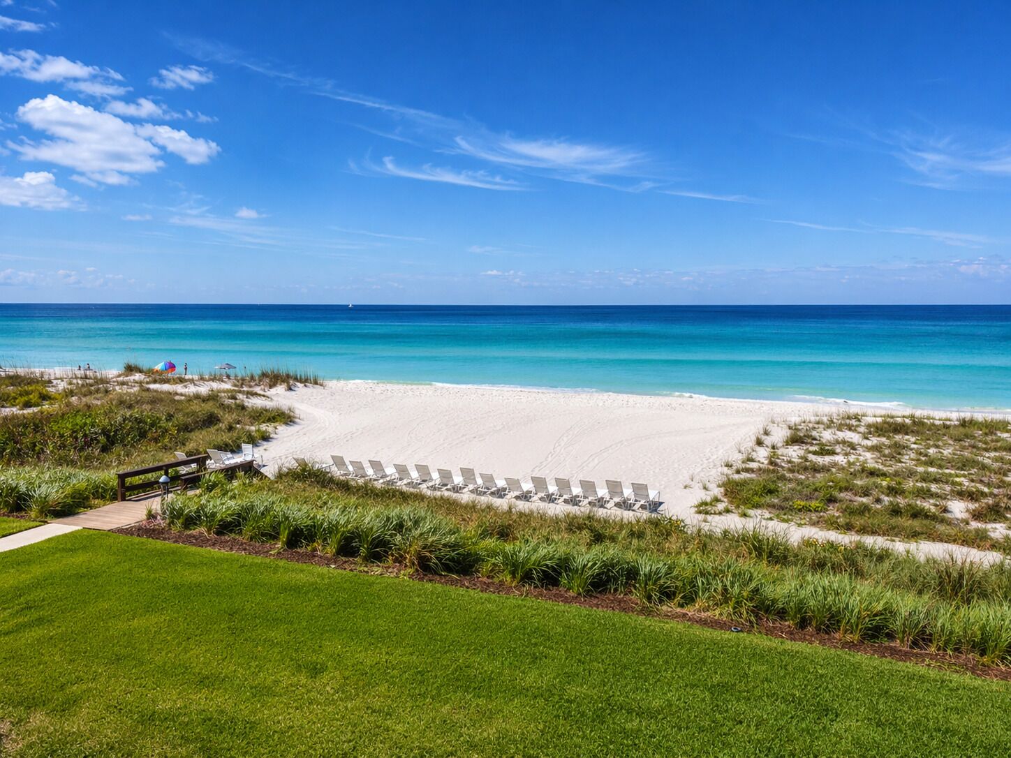 A beach with white sand, clear blue water, and a row of sun loungers.