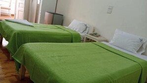 A hotel room with two beds, each covered with green bedspreads, and white pillows. There is a small bedside table with a phone and a lamp.