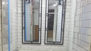 A bathroom with white tiled walls, a black and white tiled floor, a vanity with a mirror, and a blue towel rack. - De La Poste (Port Said)