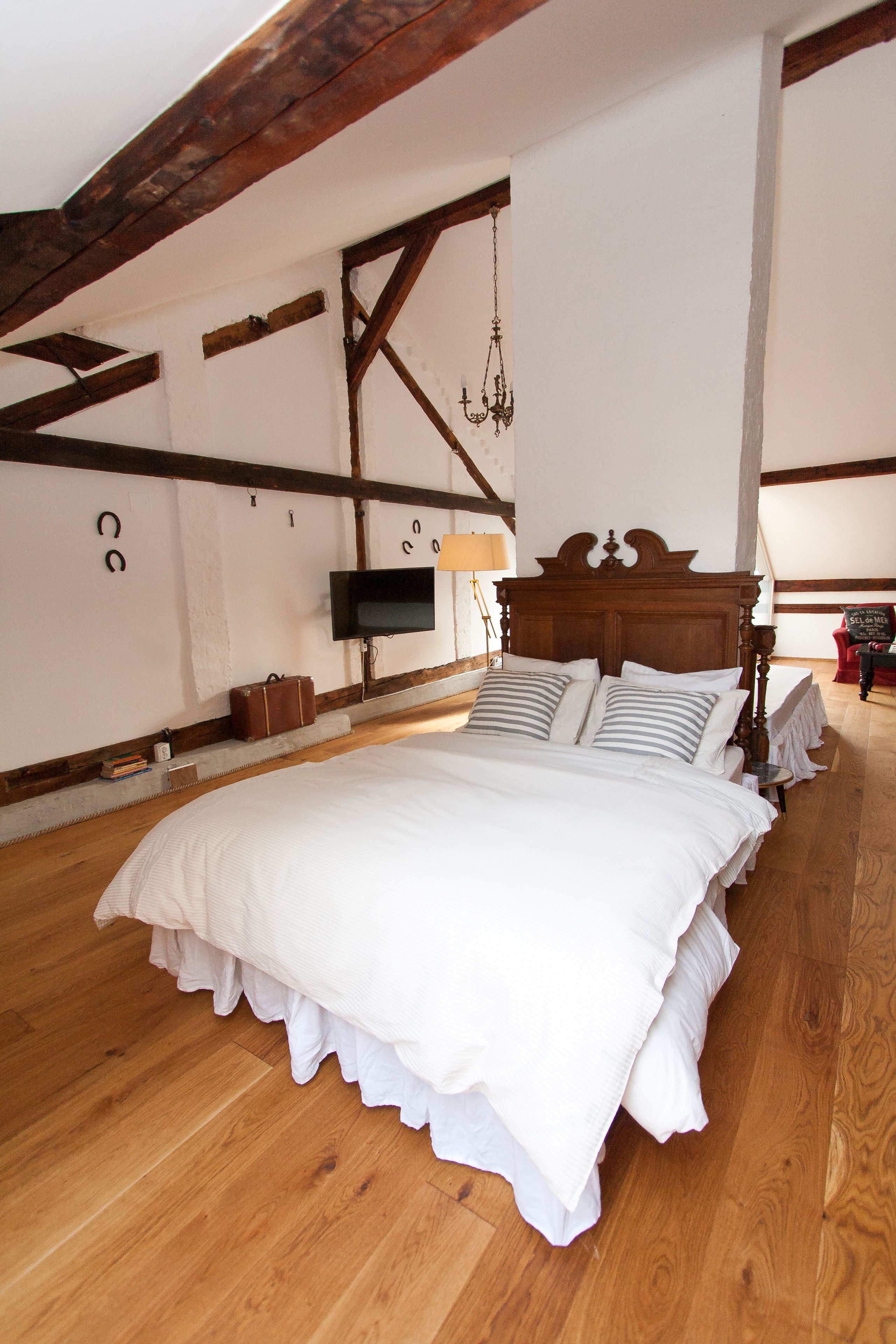 A bedroom with a wooden bed, white bedding, a TV mounted on the wall, and a chandelier.