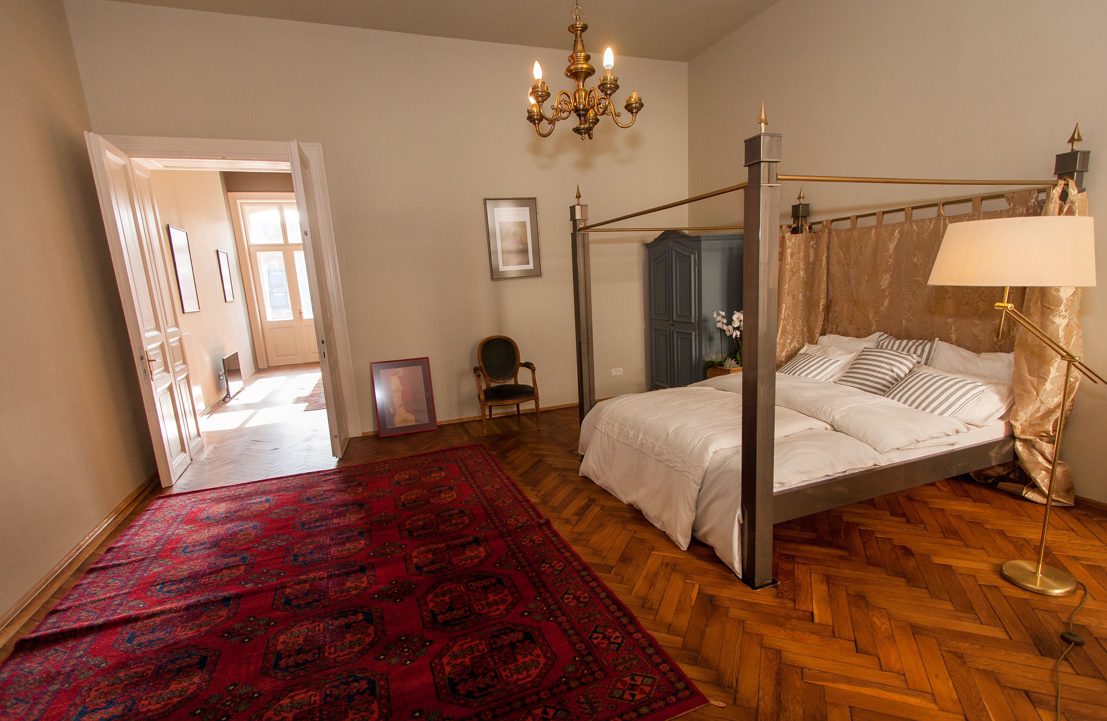 Una cama con dosel, una lámpara de pie dorada, un tapete estampado rojo y un candelabro.