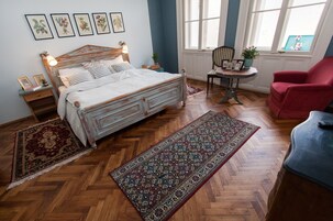 Un dormitorio con una cama de madera, un sillón rojo, una mesita con una planta y un ventanal grande.