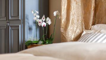 A bed with white bedding, a wicker basket with green plants, and a wall with a door and curtains.