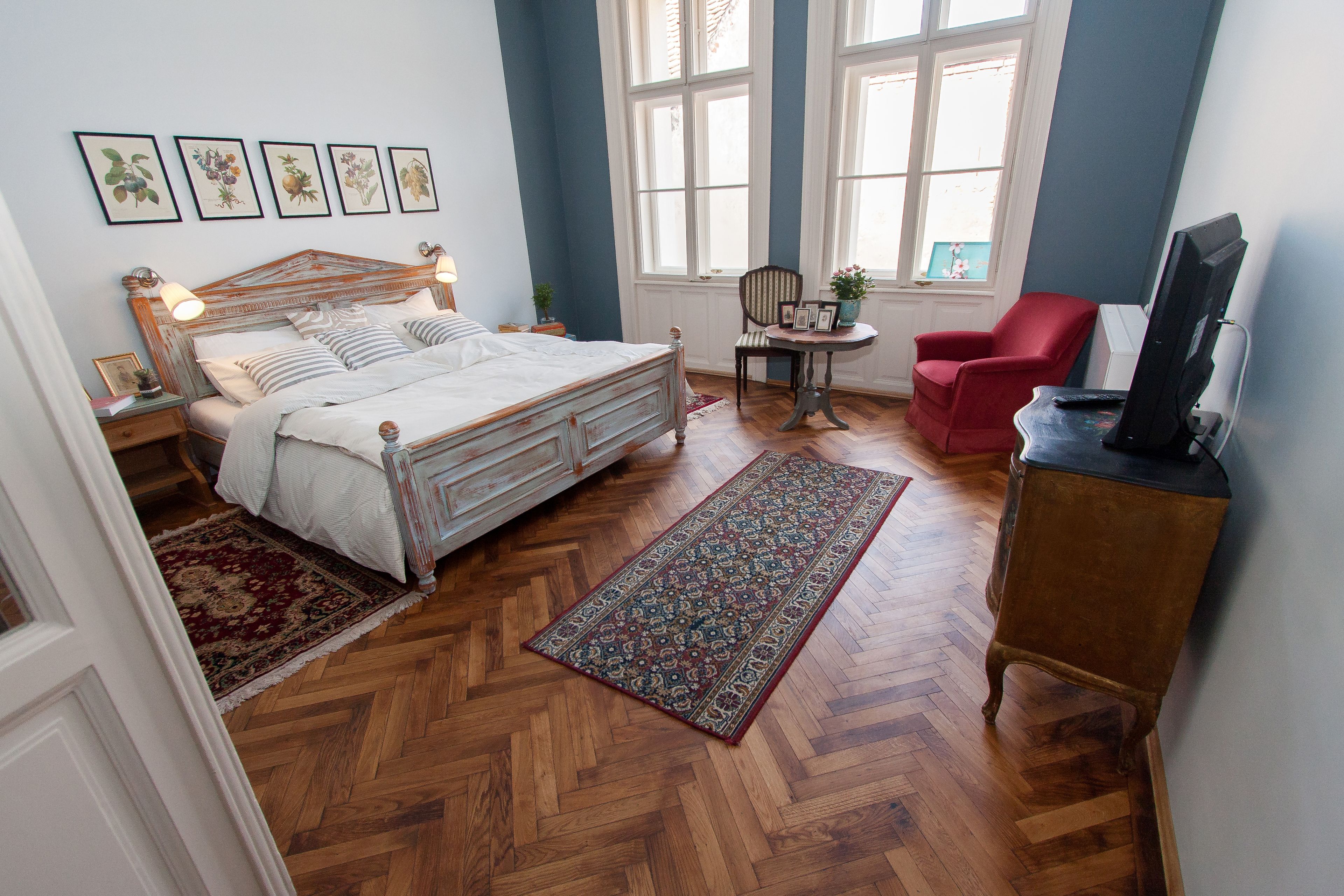 Un dormitorio con una cama de madera, una silla roja, una mesita con una planta y un televisor sobre un mueble de madera.