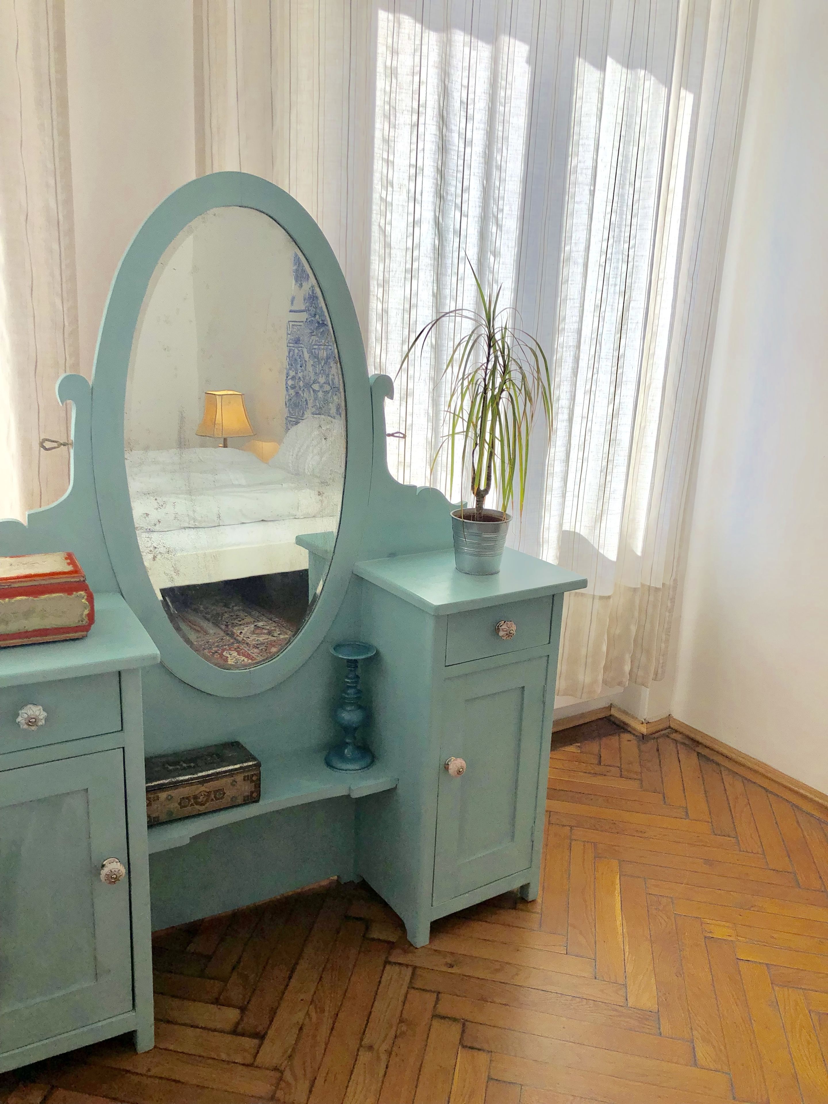 A vintage-style vanity with a large mirror, a potted plant, and a lamp.