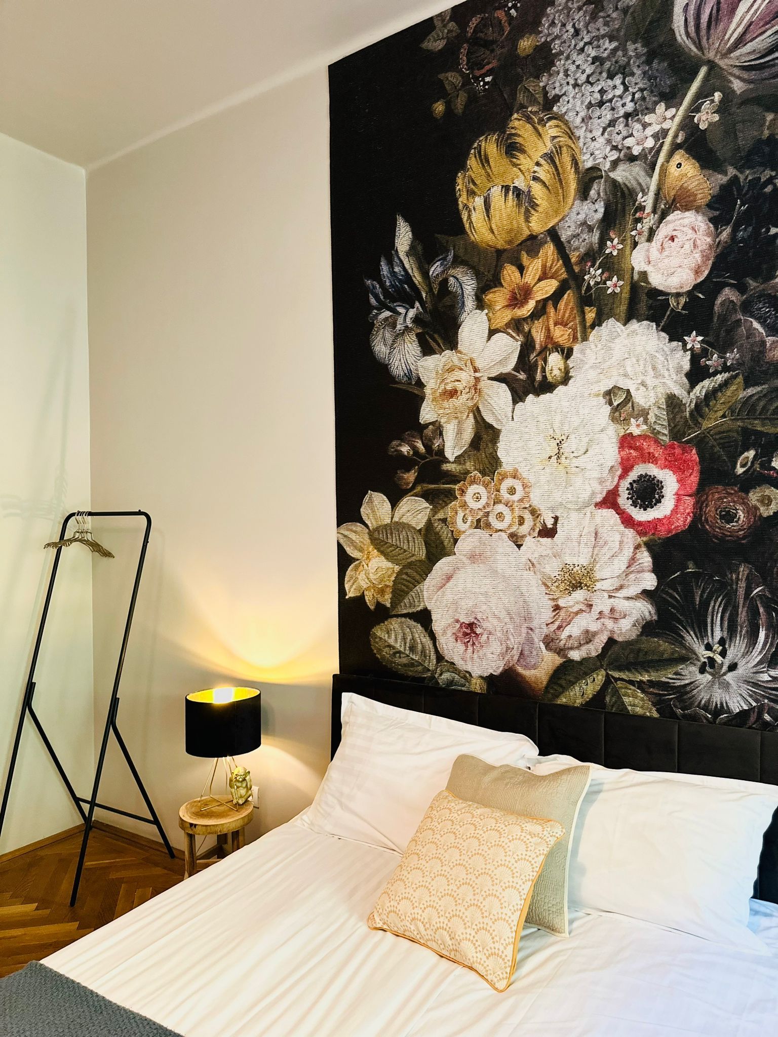 Une chambre à coucher avec un lit, des oreillers, une table de chevet, une lampe et une tapisserie murale.