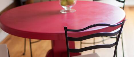 Una mesa redonda roja con un florero de vidrio que contiene flores rosadas y manzanas verdes.