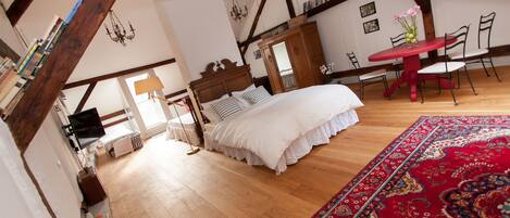 A bedroom with a wooden ceiling, a bed with white bedding, a red table with chairs, and a red carpet.