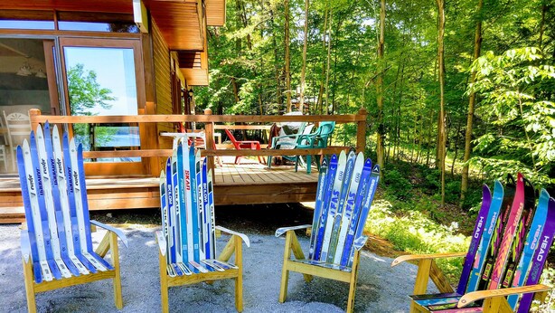 A wooden deck with a fire pit, surrounded by colorful Adirondack chairs. - Lakefront spacious contemporary. Large families welcome. Ski GORE nearby! (Chestertown)