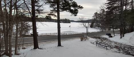 A snowy landscape with a road, trees, and a body of water.