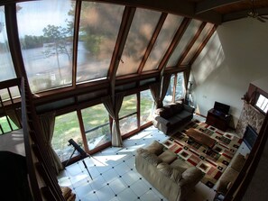 A spacious living room with large windows, a cozy sofa, a television, and a stone fireplace.