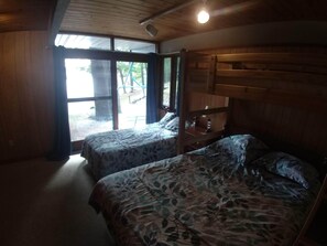 Une chambre avec deux lits, des murs en bois, une grande fenêtre et un luminaire au plafond.