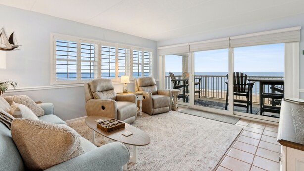 A spacious living room with a large sliding glass door leading to a balcony with a view of the sea. - Beach Condo Miles-long Views Sand and Sea, Access to Private Fishing Pier by RedAwning (Fernandina Beach)