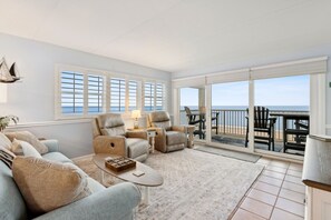 A spacious living room with a large sliding glass door leading to a balcony with a view of the sea. - Beach Condo Miles-long Views Sand and Sea, Access to Private Fishing Pier by RedAwning (Fernandina Beach)