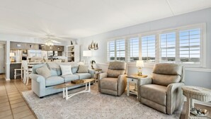 A spacious living room with a light blue sofa, beige armchairs, a coffee table, and a dining area in the background. - Beach Condo Miles-long Views Sand and Sea, Access to Private Fishing Pier by RedAwning (Fernandina Beach)