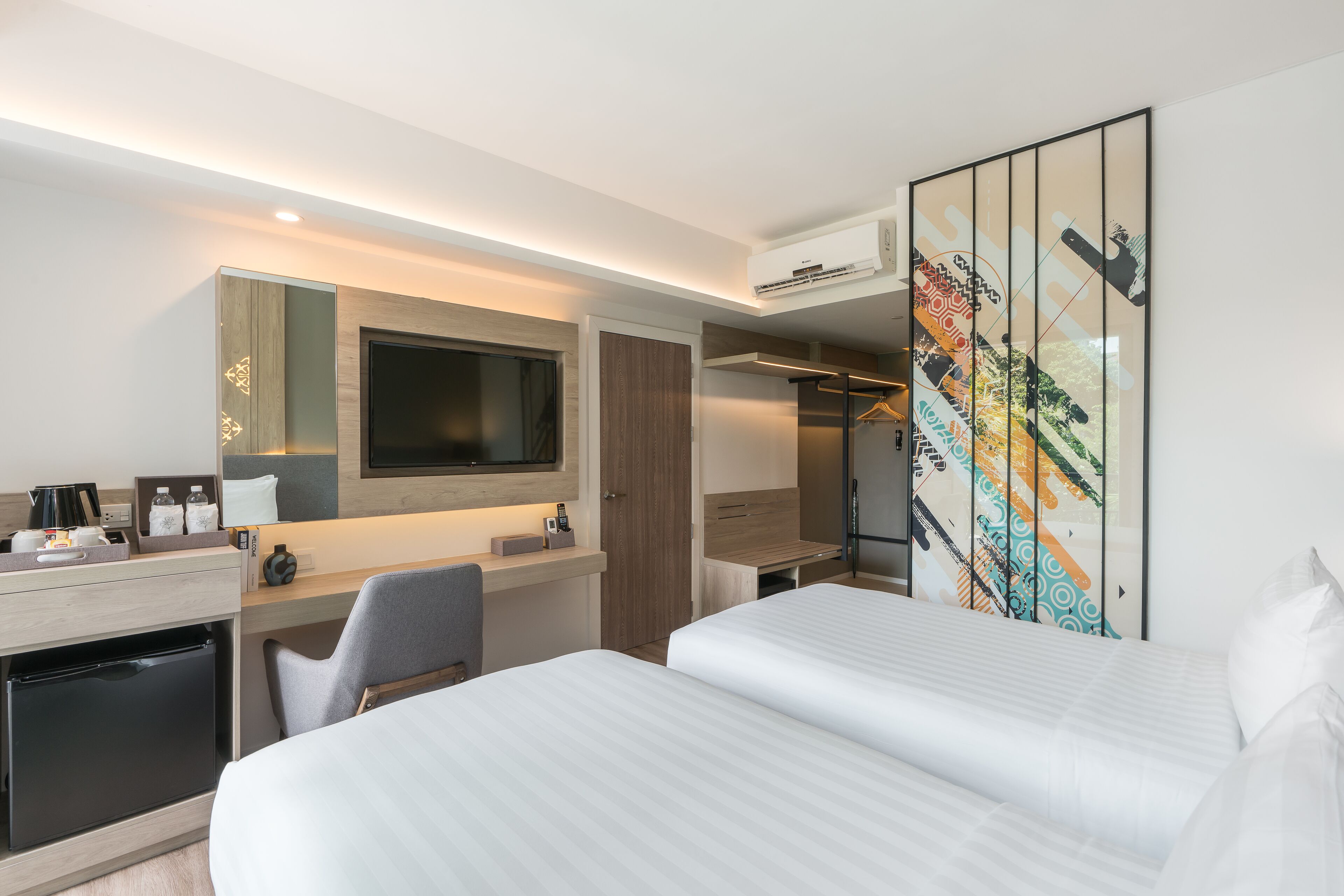 Una habitación de hotel moderna con una cama grande, un escritorio con ordenador, un televisor de pantalla plana y un armario.