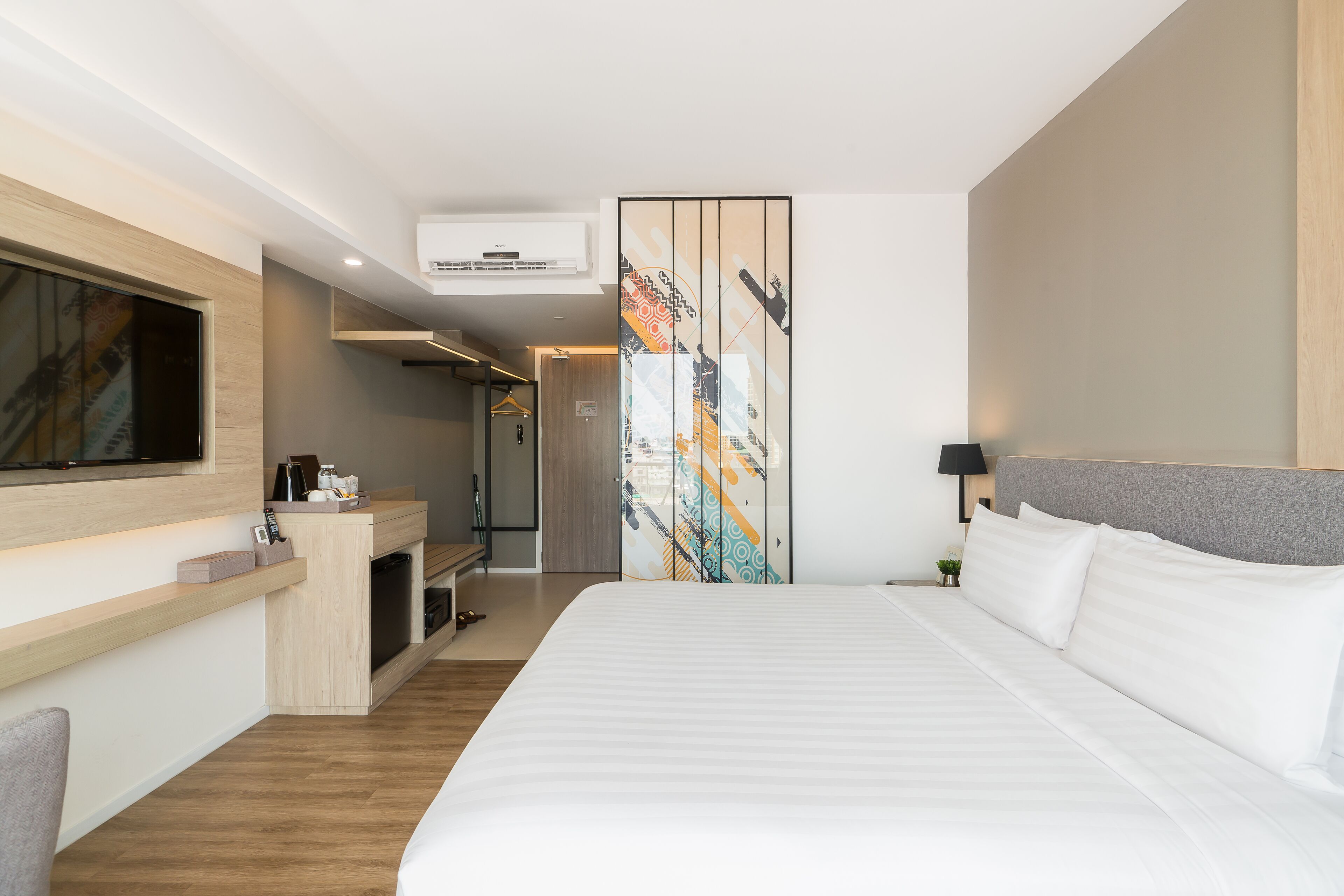 A hotel room with a large bed, a TV mounted on the wall, a desk with a computer, and a wardrobe with a colorful design.