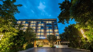 Een modern hotel met een glazen gevel, omringd door weelderige begroeiing.