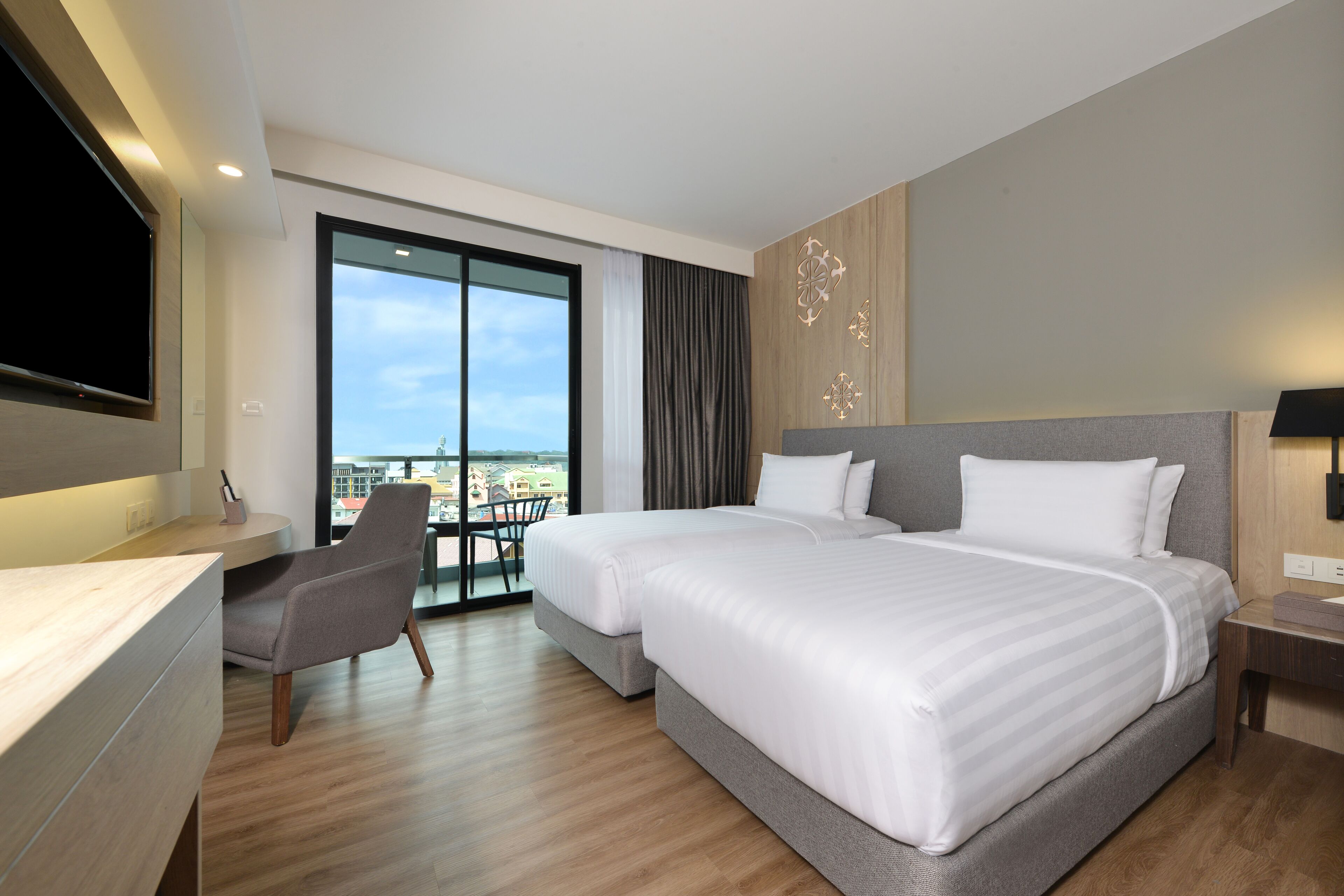 A modern hotel room with a large bed, a desk, and a chair. There is a large window with a view of the city.