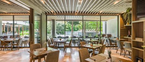 A modern restaurant with wooden tables and chairs, large windows, and a ceiling with wooden slats.