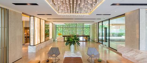 A spacious lobby with a modern chandelier, seating area, and large windows offering a view of greenery.