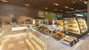 Een buffetgedeelte met diverse foodstations, waaronder een glazen vitrine met gebak en een saladebar.