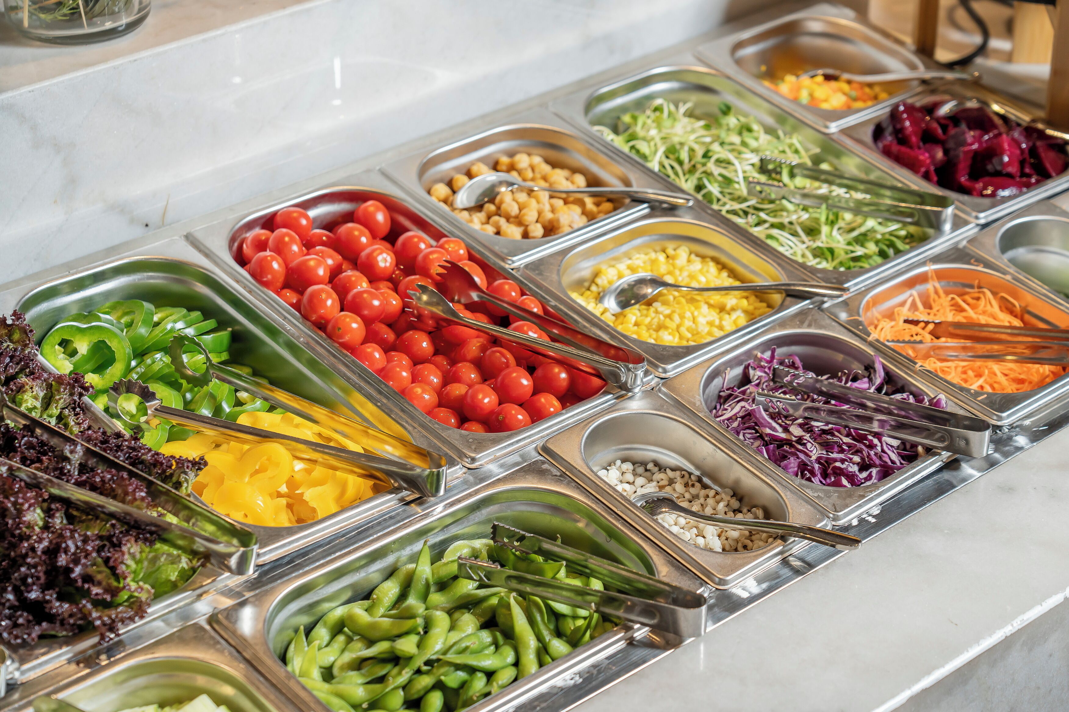 A buffet with various food options including vegetables, fruits, and grains.