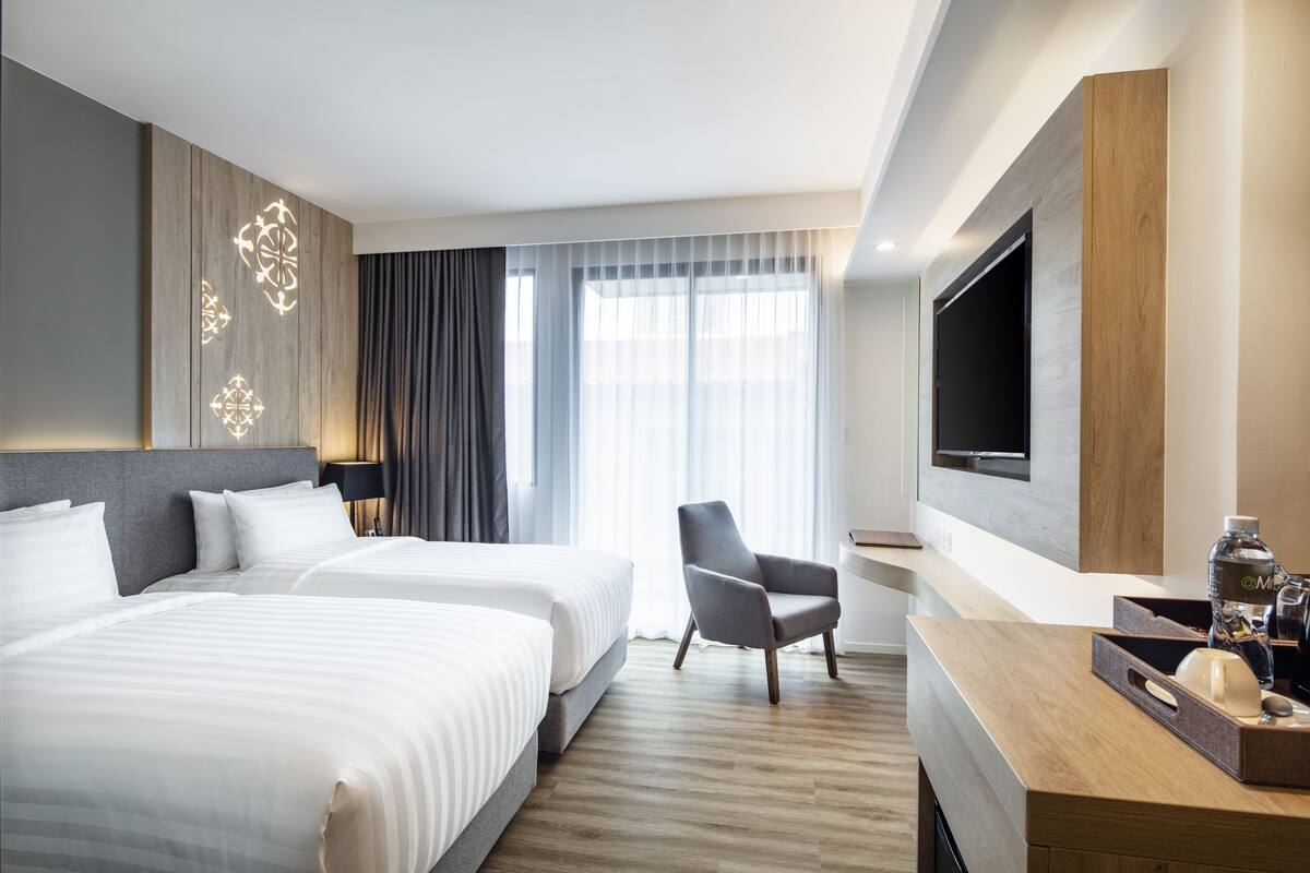 Ein Hotelzimmer mit zwei Betten, einem Fernseher, einem Schreibtisch mit Kaffeemaschine und einem Sessel.