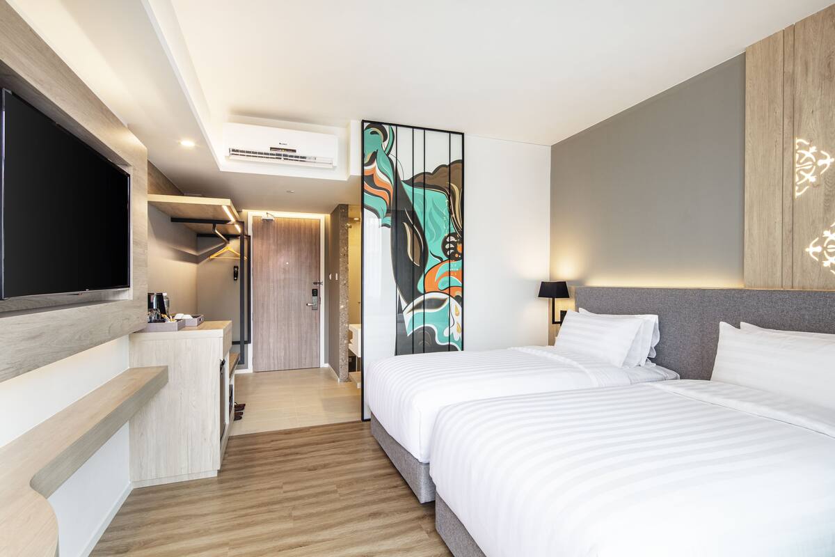 Ein modernes Hotelzimmer mit einem großen Bett, einem flachbildfernseher an der Wand, einem Schreibtisch mit Stuhl und einem dekorativen Wandbild.