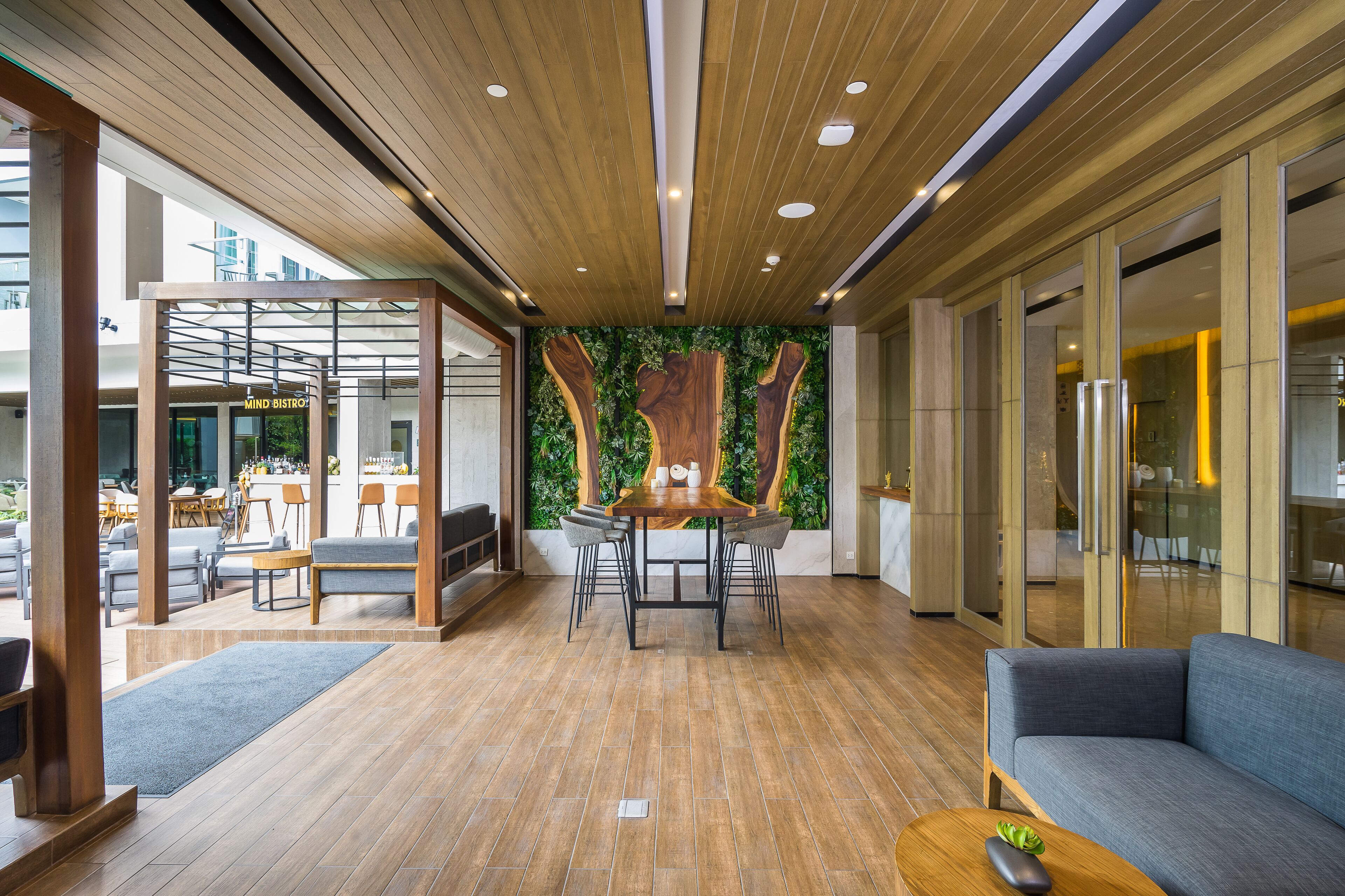 A modern interior with a wooden ceiling, a dining area with a wooden table and chairs, and a grey sofa.